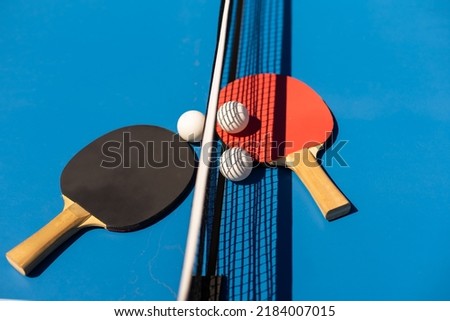 Table tennis rackets and a white plastic ball on a blue background.