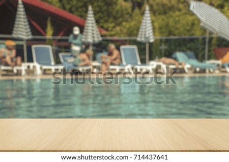 Table top and blurred background.  Big Olympic swimming pool in the open air. Ripples on the surface of turquoise water. Sun loungers and umbrellas around the pool, people sunbathe and swim.
