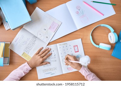 Table Top Closeup View Of Kid Student Hands Writing Doing Math Homework Exercises In Notebook With Book On Table. Learning Classes For Elementary School Pupils. Study At Home Classroom Concept.