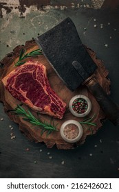 Table Top Of Uncooked Bloody Steak On Old Wooden Chopping Board With Colorful Pepper And Himalayan Salt, Rosemary And Cleaver Knife On Top 