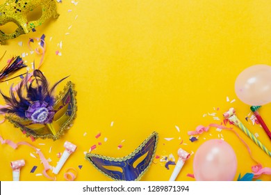 Table top view aerial image of beautiful colorful decorations carnival festival background.Flat lay accessory object the mask & decor confetti and pink balloon on modern yellow paper.copy space.
