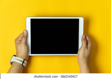 Table Top View Aerial Image Of Accessories Office Desk Background Concept. Flat Lay Of Hand Holding On White Tablet On Modern Rustic Yellow Paper And Space.