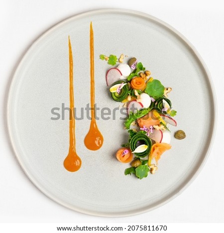 Table top view of minimalist and elegant fine dine smoked salmon salad on grey ceramic plate. Appetiser with courgette, nasturtiums, radish, capers and walnuts.
