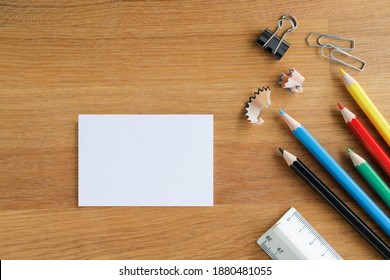 Table Top View, On A Wooden Desk Lay Down Multi Colored Pencils, Clips And A White Card, Table Top With Space For Text