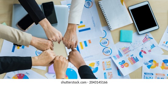 Table Top View Of A Wooden Conference Table With Charts And Graphs Papers On The Table And Six Business Women's Hands Put Together Cheering. Concept For Business Meeting.