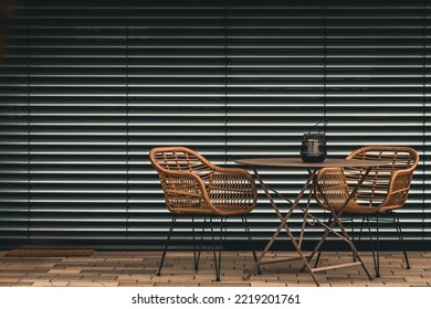 Table with two chairs on a terrace in front of blinds. Urban or industrial style.