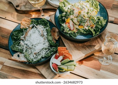 A table with two plates of food, one with a salad and the other with a sandwich. There are also two wine glasses on the table - Powered by Shutterstock - Get 15% off with code: PIKWIZARD15