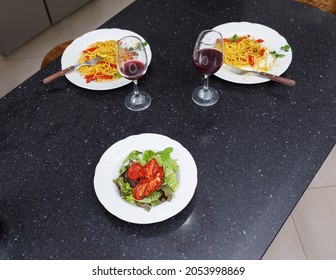 Table With Two Plates Of Pasta, A Couple Of Glasses Of Red Wine And A Platter Of Salad. Vegan Food. Couple's Dinner Concept. No People.