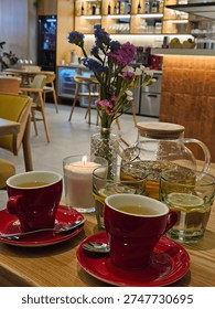 Table with two red cups and a vase of flowers. The cups are filled with tea and lemonade