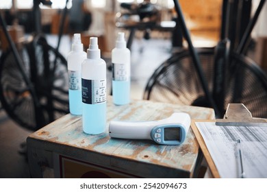 Table, virus and sanitizer with thermometer for temperature, screening and equipment for wellness. Closeup, scanner and spray bottle with clipboard for information, safety and prevent bacteria in gym - Powered by Shutterstock