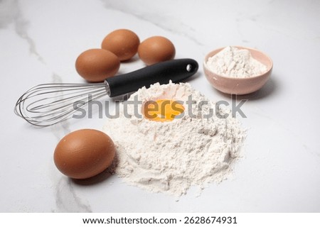 A table with a white marble surface with the necessary baking utensils, eggs rolled in flour, a whisk nearby - the perfect background for the recipe.