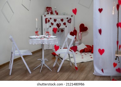 Table With White Tablecloth. Romantic Candlelight Dinner. White Fireplace Decorated With Red Hearts For Valentine's Day