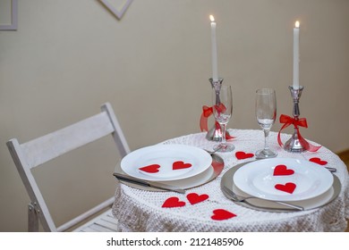 Table With White Tablecloth. Romantic Candlelight Dinner. White Fireplace Decorated With Red Hearts For Valentine's Day