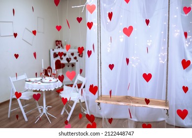 Table With White Tablecloth. Romantic Candlelight Dinner. White Fireplace Decorated With Red Hearts For Valentine's Day