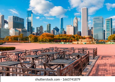 Tables And Chairs In The Grant Park Bricked Area Sit In Front Of The Buckingham Fountain And Trees In Fall Color, All In Front Of A Panorama Of The Skyline Of Chicago, Illinois