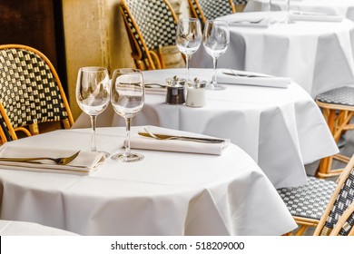 Tables With White Tablecloth And Chairs In Restaurant, Glasses And Goblet On Table.