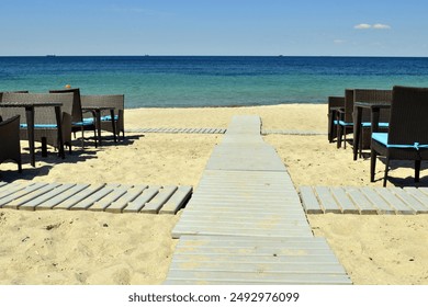 tables and a wooden walkway to the sea. A wooden walkway leading from the beach to the sea with a bright blue sky. hot summer, blue warm sea. rest, vacation - Powered by Shutterstock