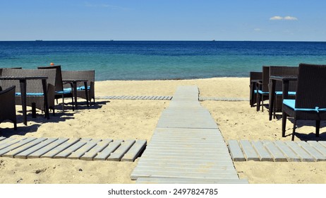 tables and a wooden walkway to the sea. A wooden walkway leading from the beach to the sea with a bright blue sky. hot summer, blue warm sea. rest, vacation - Powered by Shutterstock