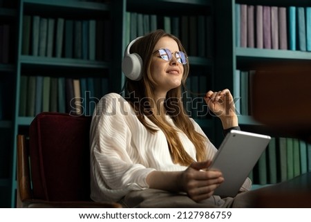 Tablet audiobook woman wireless headphones, office workplace report place. A student with glasses in the library.