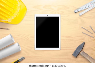 Tablet With Blank Screen For Mockup On Architect Desk. Helmet, Tools And Plans Beside. Top View.