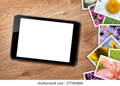 Tablet with blank screen and stack of printed pictures collage on wooden table
