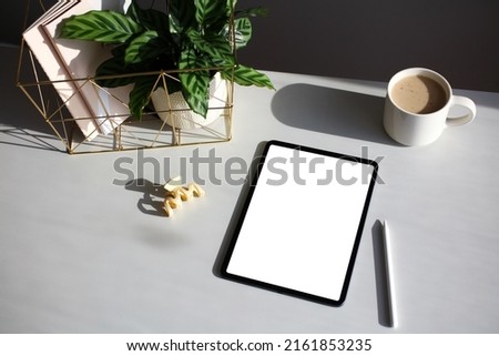 Tablet with blank screen template, digital pen, cup of coffee and female accessories. Elegant feminine workspace in sunlights.