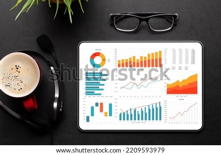 Tablet with business reports and charts, coffee cup and office supplies on desk. Top view flat lay