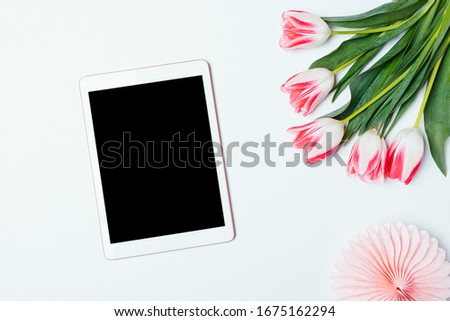 Tablet computer with empty display next to bouquet of tulip flowers on white desk, flat lay.