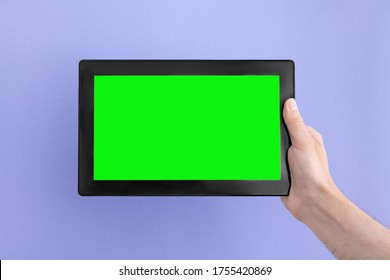 Tablet computer with green screen in man's right hand on an lilac background.