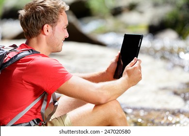 Tablet Computer Man Hiker Hiking In Yosemite, USA Using Travel App Or Map During Hike, Resting By River. Caucasian Male Hiker Relaxing On A Summer Day.