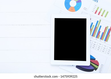 Tablet computer and papers with graph and charts on wooden table