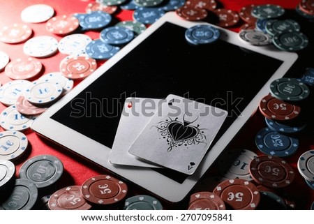 Tablet computer with poker chips and playing cards on red table in casino, closeup