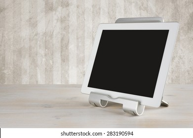 Tablet Computer In The Stand On Table Over Grunge Wall