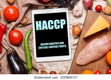 Tablet computer with text HAZARD ANALYSIS AND CRITICAL POINTS and fresh products on white wooden background