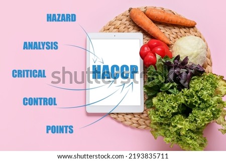 Tablet computer with text HAZARD ANALYSIS AND CRITICAL POINTS and fresh vegetables on pink background