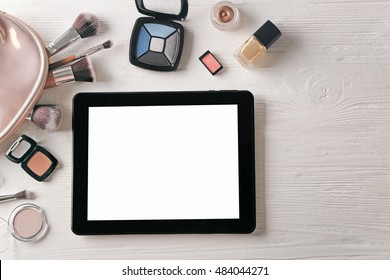 Tablet and cosmetics on wooden background