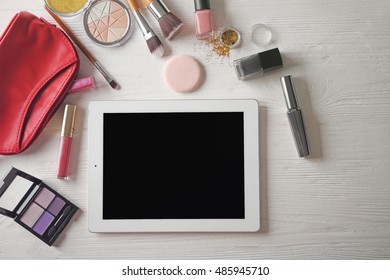 Tablet and cosmetics on wooden background