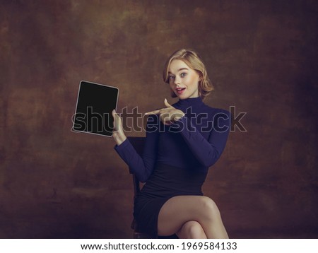 Tablet, digital. Young woman in art action isolated on brown background. Retro style, comparison of eras concept. Beautiful female model like legendary chess player, queen or duchess, old-fashioned.