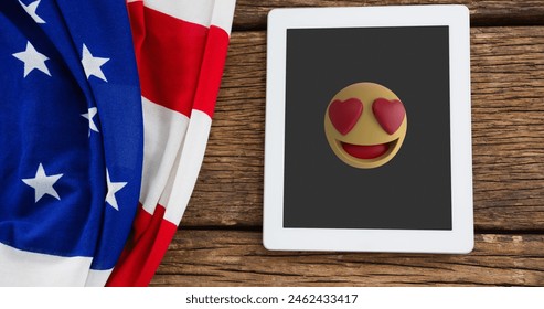 A tablet displaying heart-eyes emoji rests on a wooden surface. An American flag drapes beside tablet, adding a patriotic touch - Powered by Shutterstock