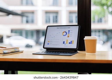 Tablet is displaying a report data graph white screen for your advertisement on a work desk with a notebook and a pen near a window
