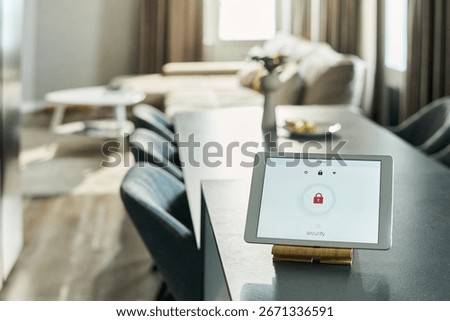 Tablet displaying security lock screen standing on kitchen counter in modern home interior, sunlight streaming through window, living room with sofa and table visible in background
