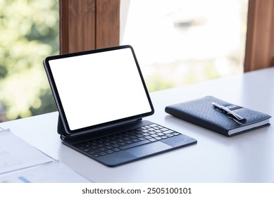 Tablet is displaying a white screen for your advertisement on a work desk with a notebook and a pen near a window - Powered by Shutterstock