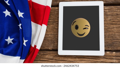 A tablet displaying winking emoji rests beside American flag. Wood planks form background, adding a rustic touch - Powered by Shutterstock
