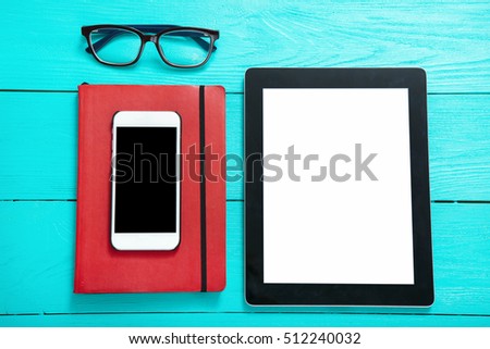 Tablet with empty screen and mobilephone with copy space on screen and education accessories on blue wooden background. Top view