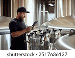 With tablet in hand, brewery technologist checking the brewing machinery, technology control of quality in beer production. Concept of beer, brewery, manufacture, quality control