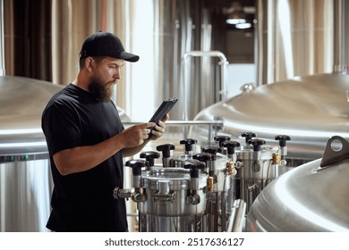 With tablet in hand, brewery technologist checking the brewing machinery, technology control of quality in beer production. Concept of beer, brewery, manufacture, quality control - Powered by Shutterstock