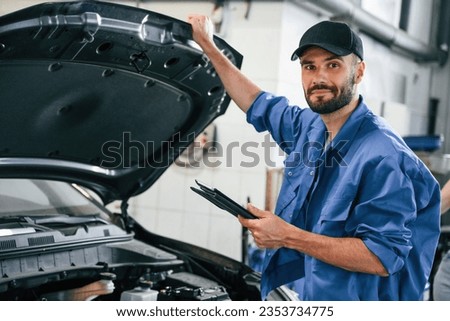 With tablet in hands. Auto mechanic working in garage. Repair service.