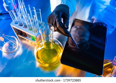 Tablet In The Hands Of The Laboratory Assistant. Few Test Tubes On The Medic's Desk. Medecine. Concept - Doctor Shows A Tablet. Epidemiology. Study Of Pneumonia. Pandemic Control Fever Investigation