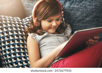 Tablet, headphones and relax with child on sofa in home living room for fun, learning on app or having fun. Toddler, technology and happy girl on couch, streaming movie or typing on social media - Powered by Shutterstock