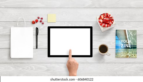 Tablet with isolated white screen for app or responsive web site design presentation. Top view of white wooden desk. Bag, gift, magazine, note, coffee beside.